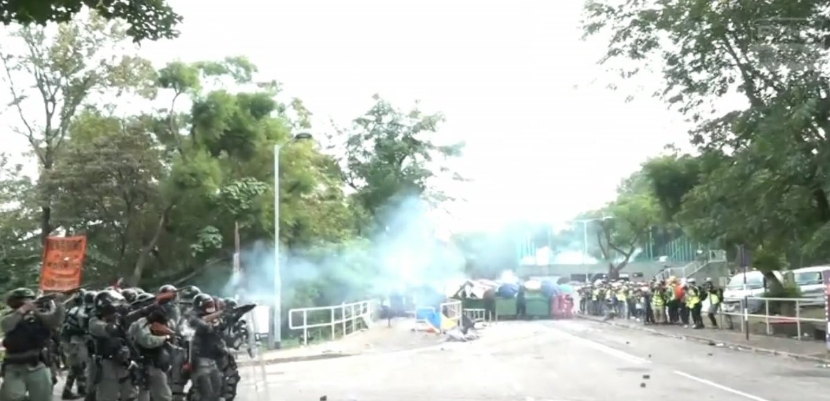 Police repeatedly fire tear gas at CUHK, as student protesters inch closer to them, hiding behind rubbish bins and umbrellas