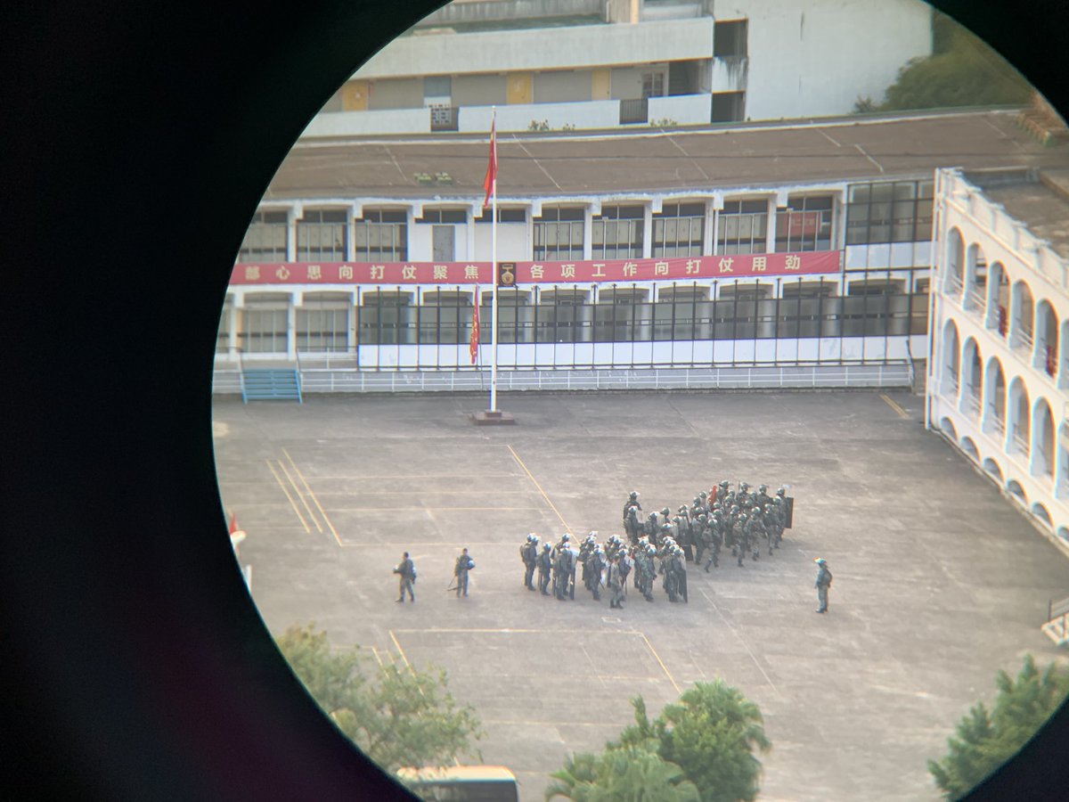 Shots of the PLA troops inside their base - as seen thru binoculars from a high perch inside PolyU - with riot shields, helmets, marching four strong, while chanting loudly #HongKongProtests